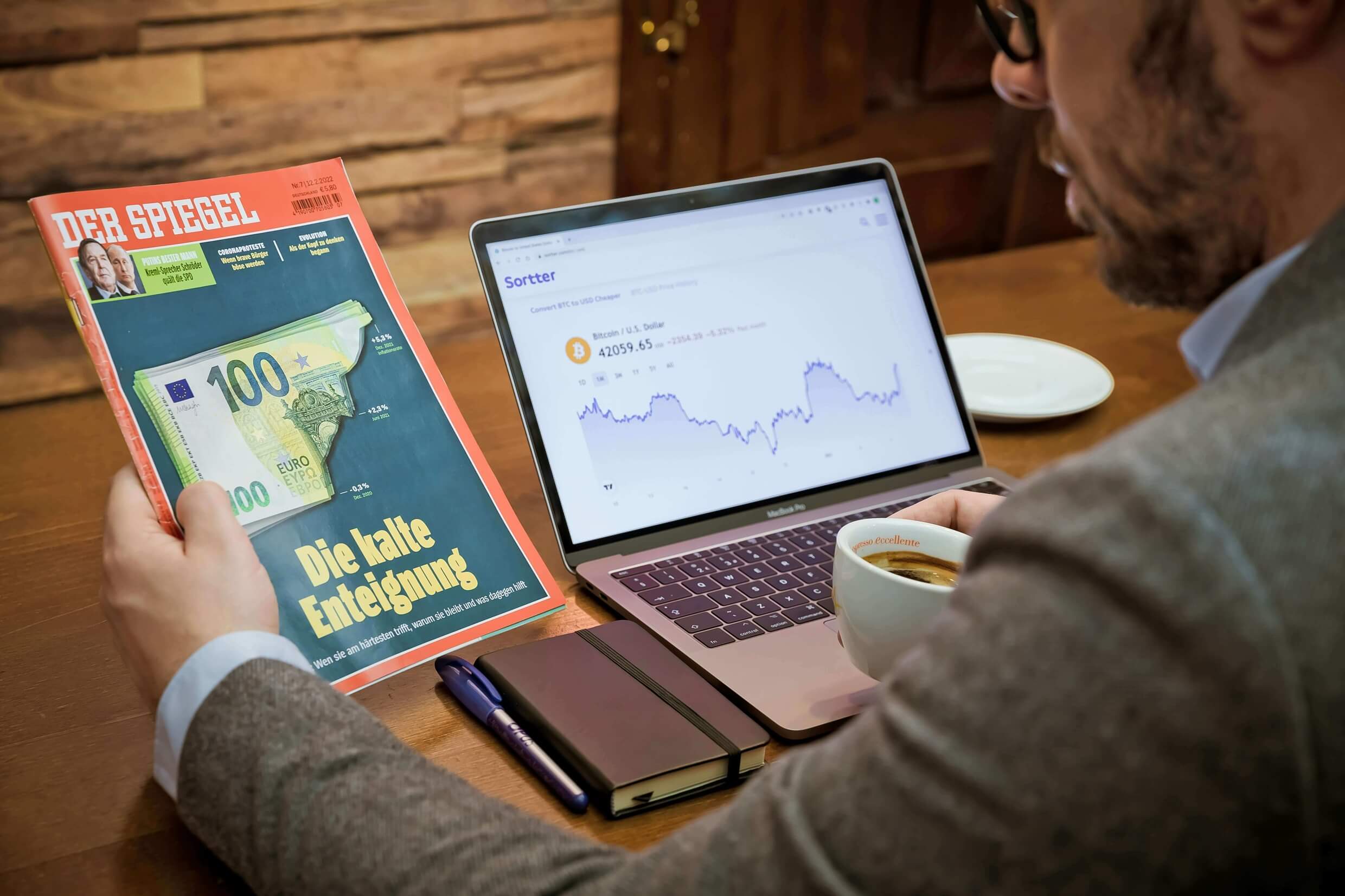 Ein Mann sitzt vor einem Laptop und hält ein Finanzmagazin in der linken Hand